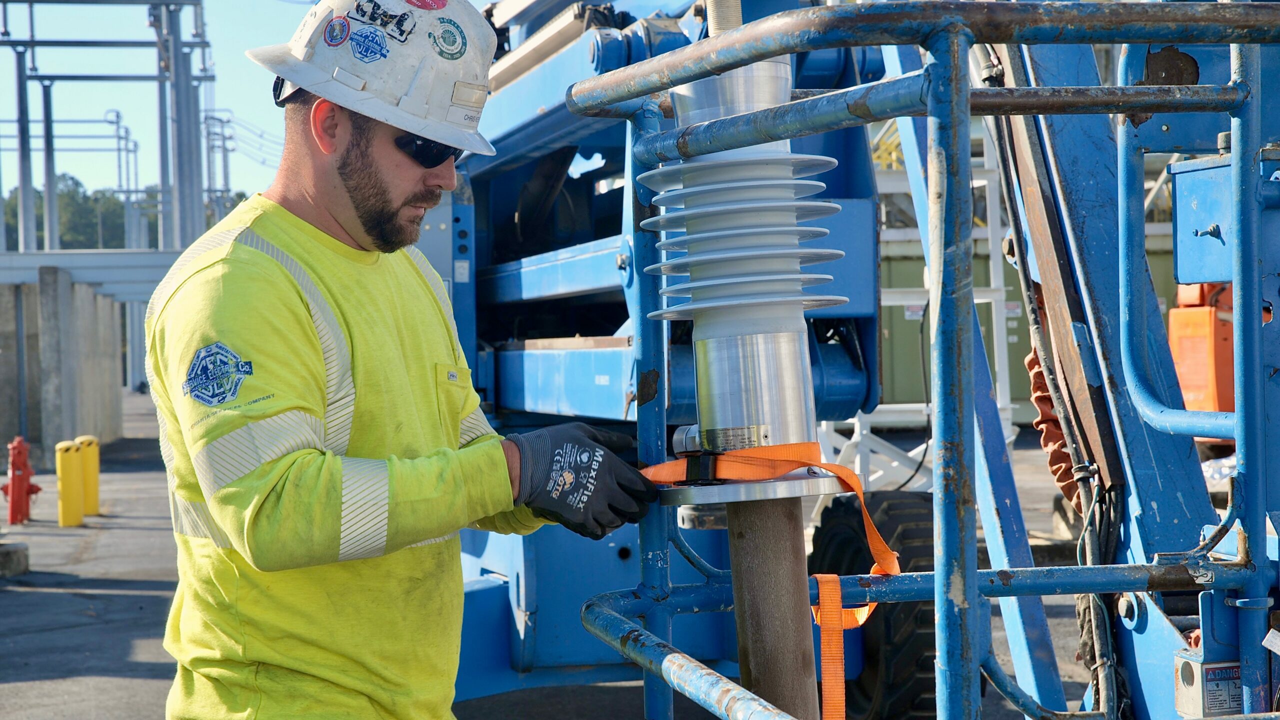 Construction worker in a neon yellow shirt and hard hat secures a large electrical insulator on blue scaffolding.